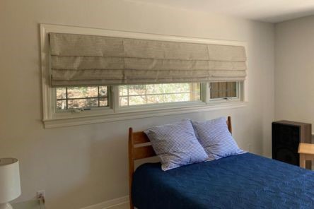 Walnut Creek bedroom window with custom Roman blinds partly raised, letting in natural light and showcasing the room’s welcoming décor.