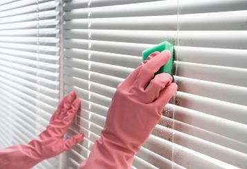 Person using a soft brush to clean fabric blinds.